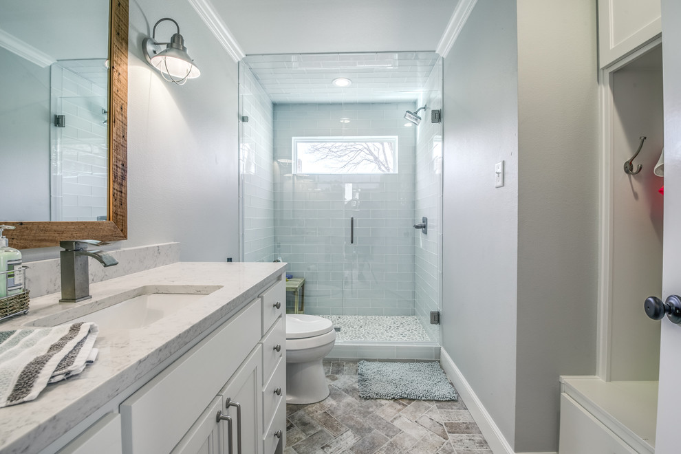 Inredning av ett lantligt mellanstort badrum med dusch, med släta luckor, vita skåp, en toalettstol med separat cisternkåpa, glaskakel, grå väggar, tegelgolv, ett undermonterad handfat och bänkskiva i kvartsit