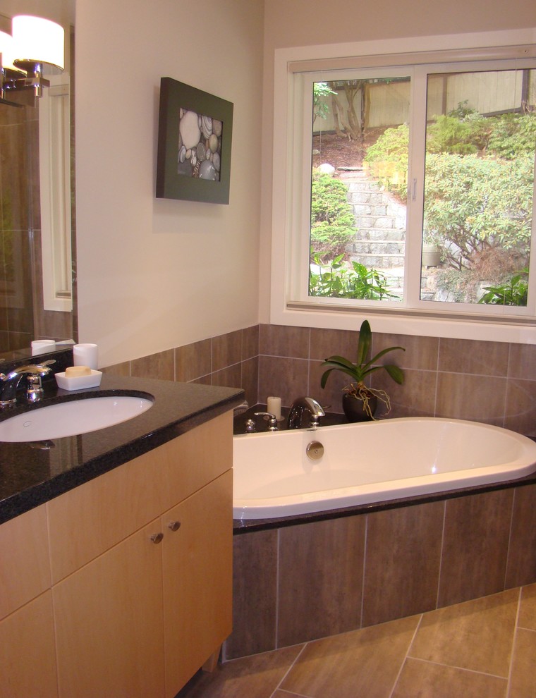 Klassisk inredning av ett mellanstort badrum, med släta luckor, skåp i ljust trä, ett platsbyggt badkar, grå kakel, porslinskakel, beige väggar, klinkergolv i porslin, ett undermonterad handfat och granitbänkskiva