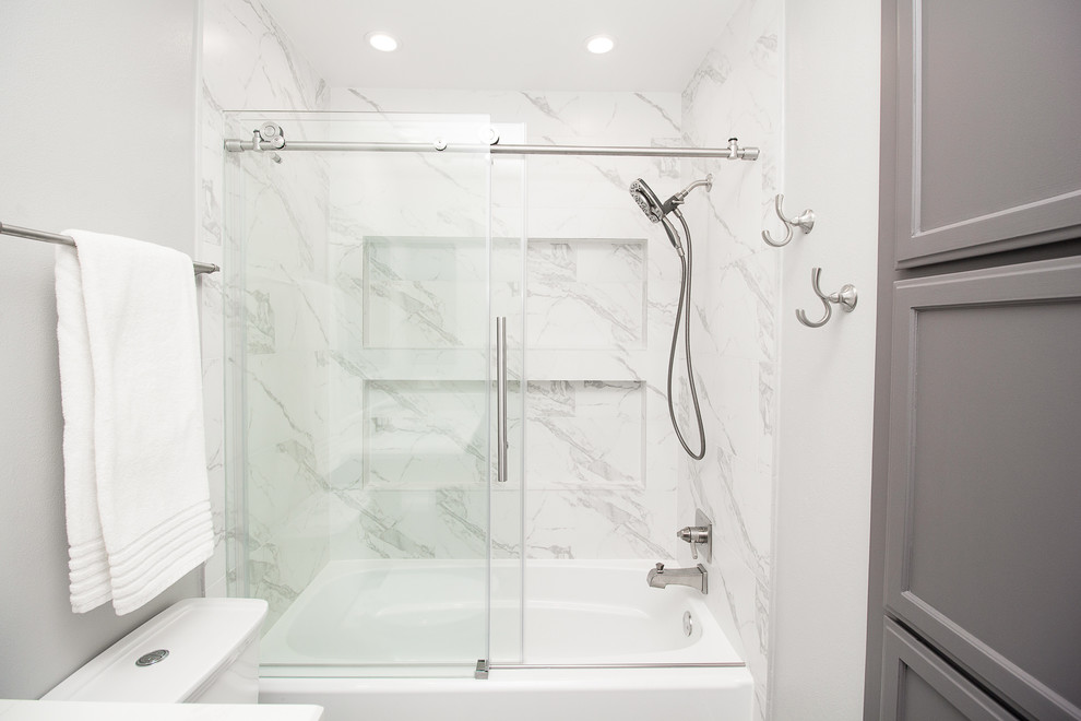 Пример оригинального дизайна: маленькая ванная комната в стиле неоклассика (современная классика) с фасадами в стиле шейкер, серыми фасадами, ванной в нише, душем над ванной, белой плиткой, керамогранитной плиткой, серыми стенами, полом из керамогранита, душевой кабиной, врезной раковиной, столешницей из искусственного кварца, серым полом и душем с раздвижными дверями для на участке и в саду