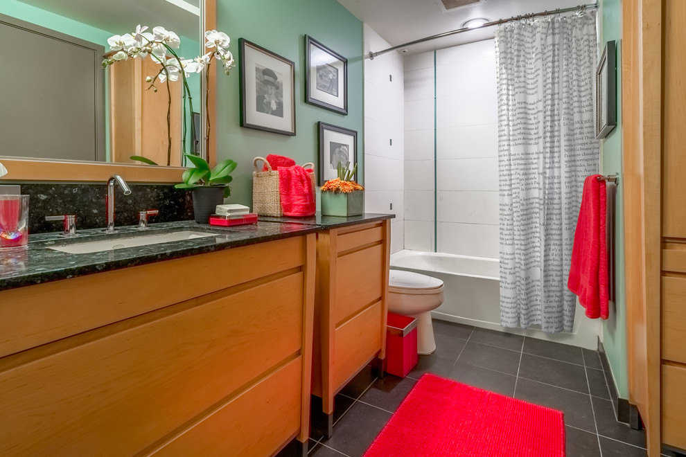 This is an example of a small contemporary ensuite bathroom in Seattle with freestanding cabinets, light wood cabinets, a shower/bath combination, a two-piece toilet, white tiles, ceramic tiles, green walls, ceramic flooring, a submerged sink, granite worktops, grey floors and a shower curtain.