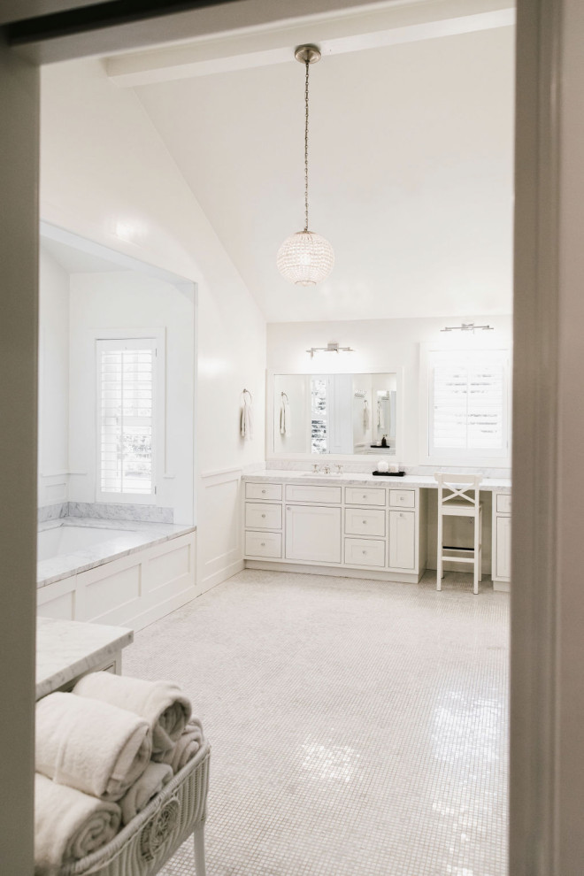 This is an example of a large country ensuite bathroom in Los Angeles with a built-in bath, white tiles, marble tiles, white walls, light hardwood flooring, marble worktops, brown floors, white worktops, double sinks, a vaulted ceiling and panelled walls.