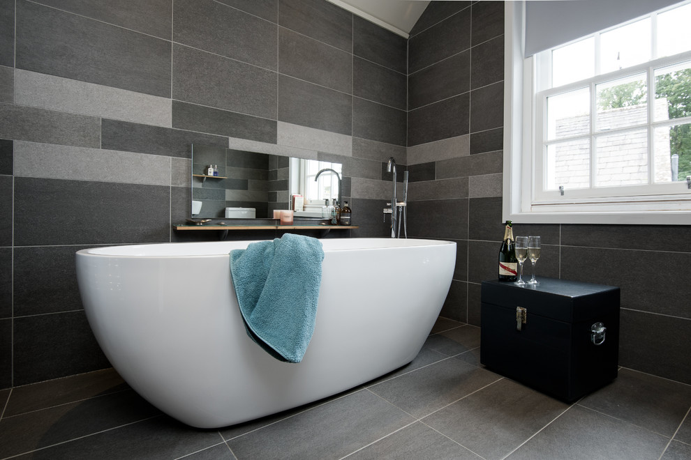 This is an example of a medium sized modern family bathroom in Other with freestanding cabinets, a freestanding bath, a one-piece toilet, grey tiles, stone tiles, grey walls, ceramic flooring and a pedestal sink.