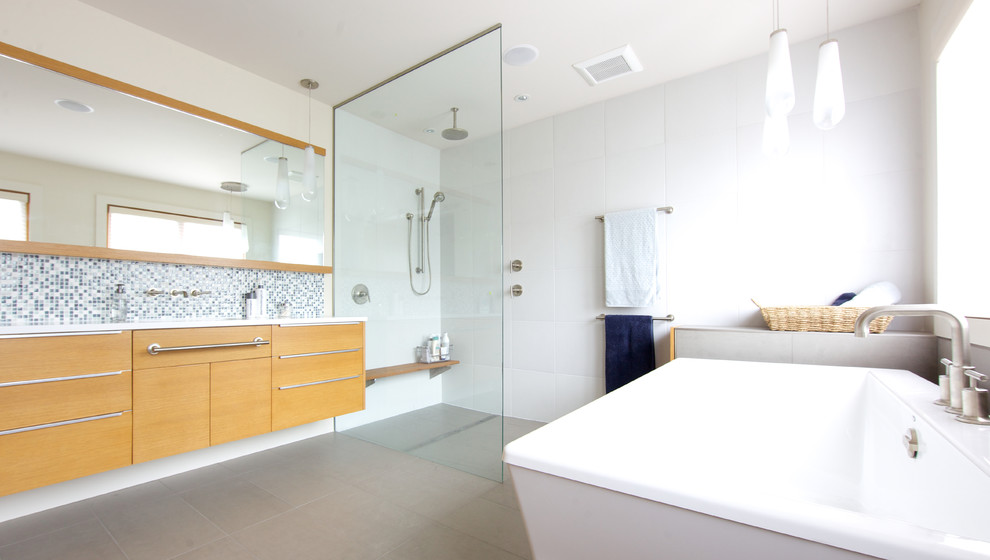 Design ideas for a large contemporary ensuite bathroom in Vancouver with flat-panel cabinets, medium wood cabinets, a freestanding bath, a walk-in shower, a two-piece toilet, white tiles, mosaic tiles, white walls, a submerged sink and porcelain flooring.