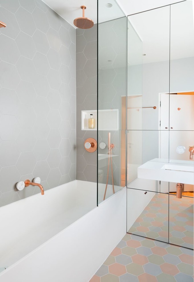 Inspiration for a small contemporary ensuite bathroom in London with grey tiles, a wall-mounted sink, an alcove bath, multi-coloured floors, an open shower, a shower/bath combination, a wall mounted toilet, grey walls and a single sink.
