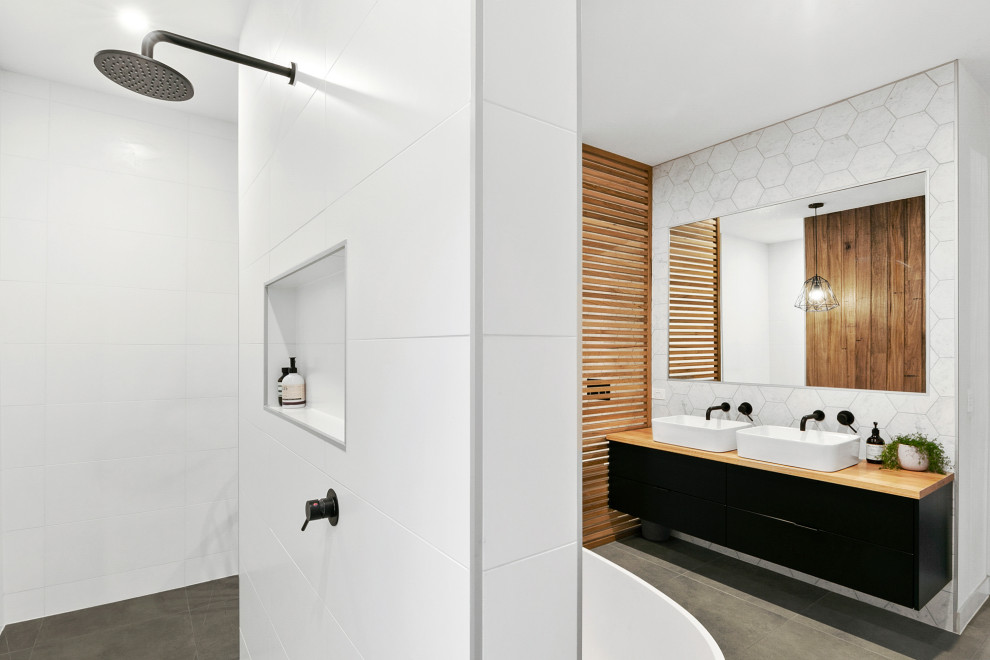 Источник вдохновения для домашнего уюта: главная ванная комната среднего размера в стиле модернизм с плоскими фасадами, черными фасадами, отдельно стоящей ванной, открытым душем, белой плиткой, керамической плиткой, белыми стенами, полом из цементной плитки, настольной раковиной, столешницей из дерева, серым полом, открытым душем, бежевой столешницей, нишей, тумбой под две раковины и подвесной тумбой