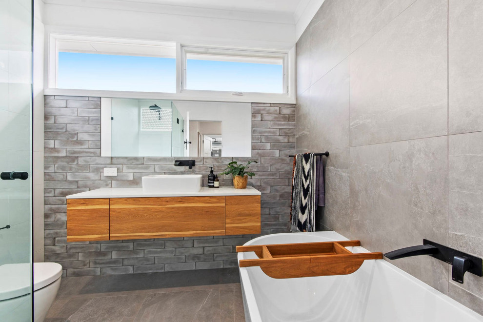 Foto di una stanza da bagno design con ante lisce, ante in legno scuro, vasca freestanding, piastrelle grigie, pareti bianche, lavabo a bacinella, pavimento grigio e top bianco