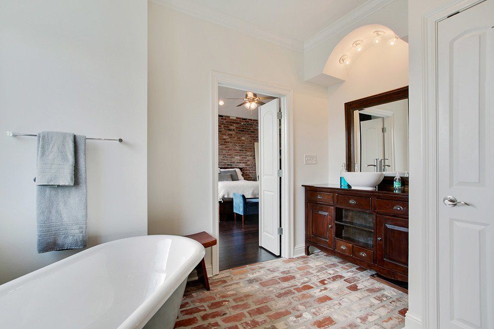 На фото: большая главная ванная комната в классическом стиле с настольной раковиной, фасадами островного типа, темными деревянными фасадами, столешницей из дерева, отдельно стоящей ванной, белыми стенами и кирпичным полом с
