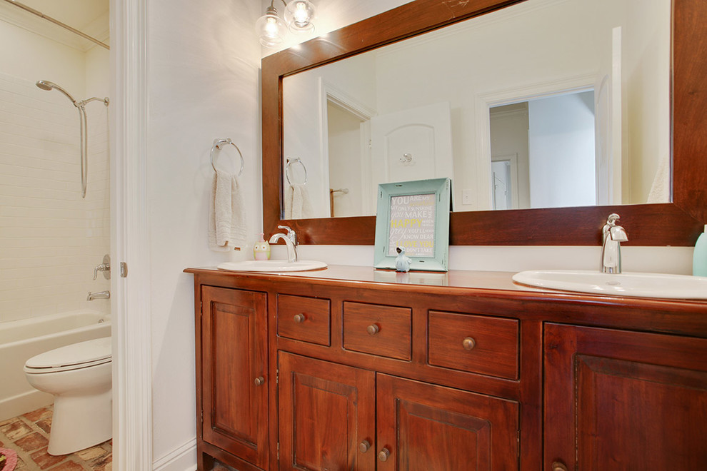 Inredning av ett klassiskt stort en-suite badrum, med ett nedsänkt handfat, släta luckor, skåp i mellenmörkt trä, bänkskiva i akrylsten, en dusch/badkar-kombination, en toalettstol med hel cisternkåpa, vita väggar och tegelgolv