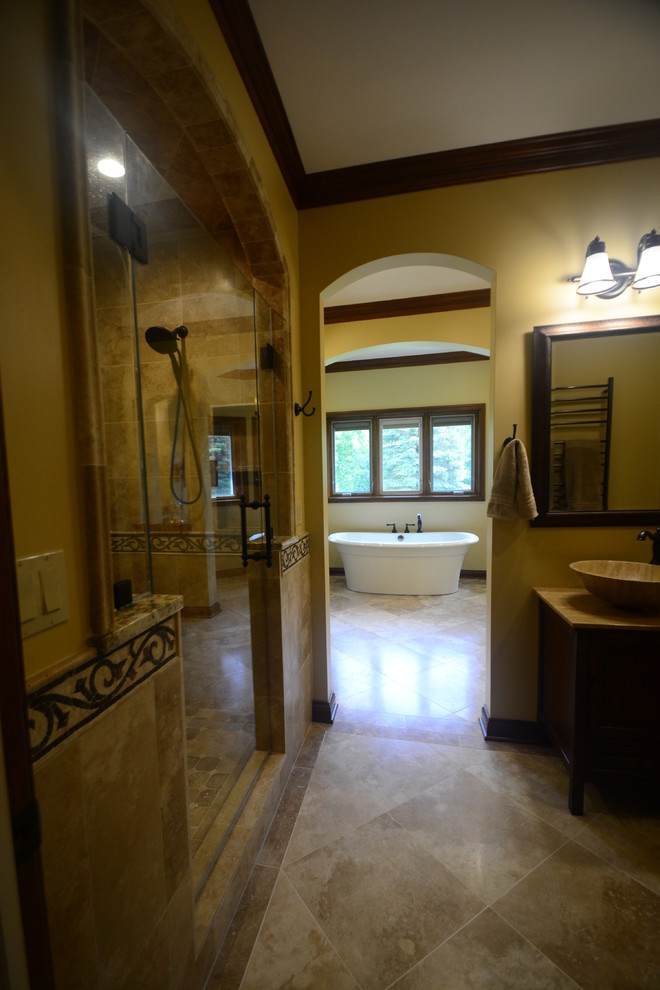 Cette image montre une très grande salle de bain principale méditerranéenne en bois brun avec un placard avec porte à panneau surélevé, une baignoire indépendante, une douche double, WC séparés, un carrelage beige, un mur beige, un sol en calcaire, une vasque, un plan de toilette en granite, un sol beige, une cabine de douche à porte battante et un carrelage de pierre.