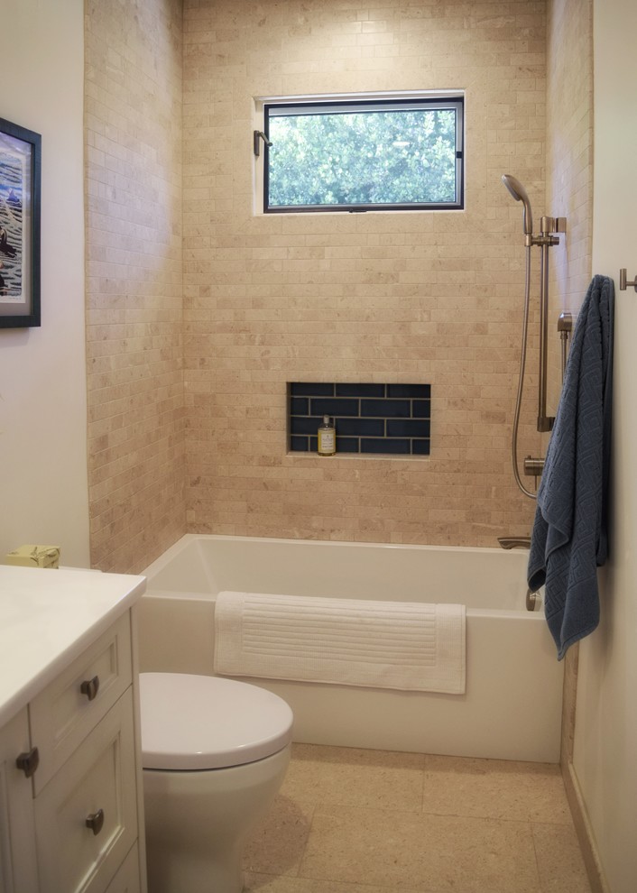На фото: ванная комната среднего размера в морском стиле с фасадами с утопленной филенкой, белыми фасадами, ванной в нише, душем над ванной, унитазом-моноблоком, бежевой плиткой, плиткой из известняка, белыми стенами, полом из травертина, врезной раковиной, столешницей из искусственного кварца, бежевым полом и шторкой для ванной