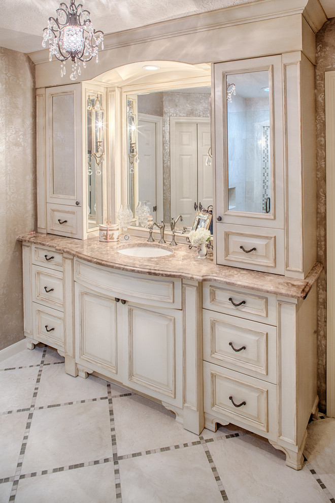 Exemple d'une salle de bain chic avec un lavabo encastré, un placard avec porte à panneau surélevé, des portes de placard beiges, un plan de toilette en marbre, WC à poser, un carrelage beige et un carrelage de pierre.