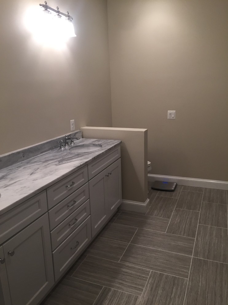 Example of a mid-sized transitional master gray tile and stone tile slate floor drop-in bathtub design in DC Metro with shaker cabinets, gray cabinets, a two-piece toilet, beige walls and an undermount sink