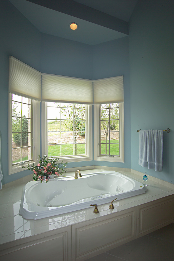 Modelo de cuarto de baño principal clásico grande con armarios con paneles con relieve, puertas de armario de madera clara, bañera encastrada, paredes azules y suelo de travertino