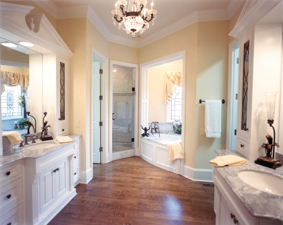 Idées déco pour une salle de bain principale classique de taille moyenne avec un placard à porte affleurante, des portes de placard blanches, une baignoire encastrée, une douche d'angle, WC séparés, un carrelage blanc, du carrelage en marbre, un mur jaune, un sol en bois brun, un lavabo encastré, un plan de toilette en marbre, un sol marron et une cabine de douche à porte battante.