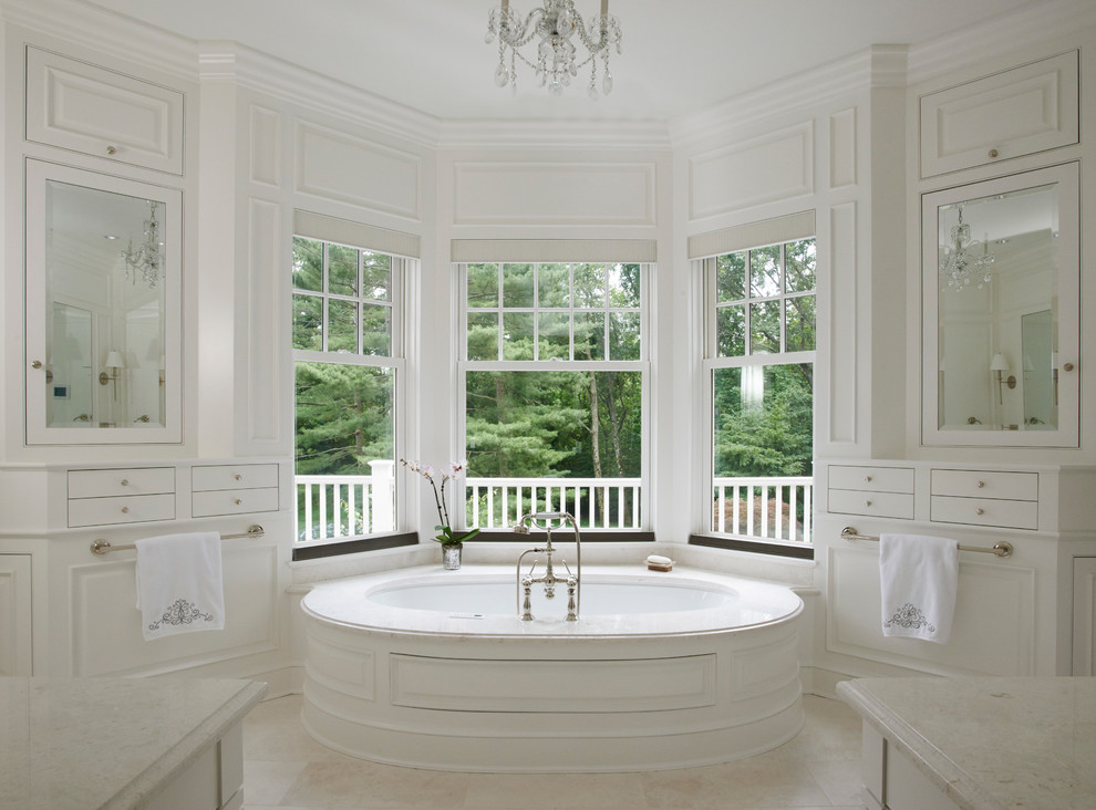 На фото: большая главная ванная комната в классическом стиле с фасадами с выступающей филенкой, белыми фасадами, полновстраиваемой ванной, полом из травертина, столешницей из известняка и бежевым полом с