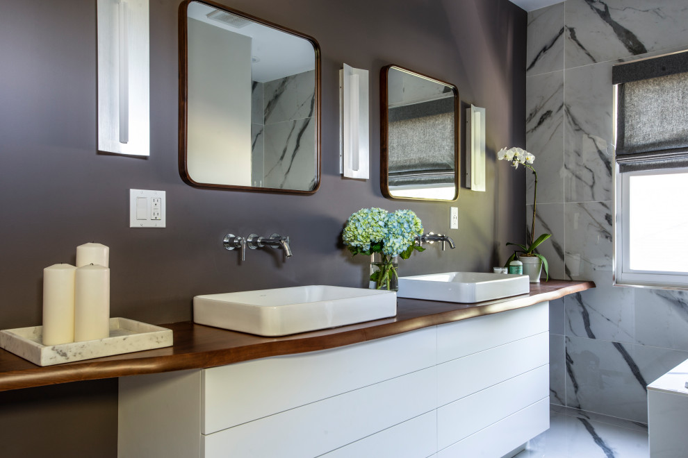 Idee per una stanza da bagno design con ante lisce, ante bianche, piastrelle grigie, pareti grigie, lavabo a bacinella, top in legno, pavimento grigio, top marrone e due lavabi