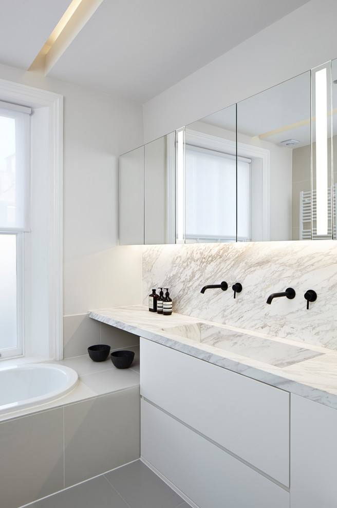 Пример оригинального дизайна: большая главная ванная комната в стиле модернизм с плоскими фасадами, белыми фасадами, накладной ванной, белыми стенами, полом из керамогранита, мраморной столешницей, серым полом, разноцветной столешницей, разноцветной плиткой, плиткой из листового камня и раковиной с несколькими смесителями