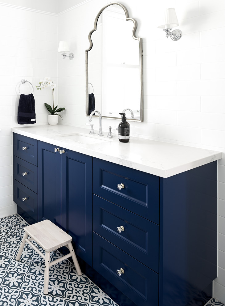 Cette image montre une salle de bain traditionnelle avec un placard avec porte à panneau encastré, des portes de placard bleues, un carrelage blanc, un mur blanc, un lavabo encastré, un sol multicolore et un plan de toilette blanc.