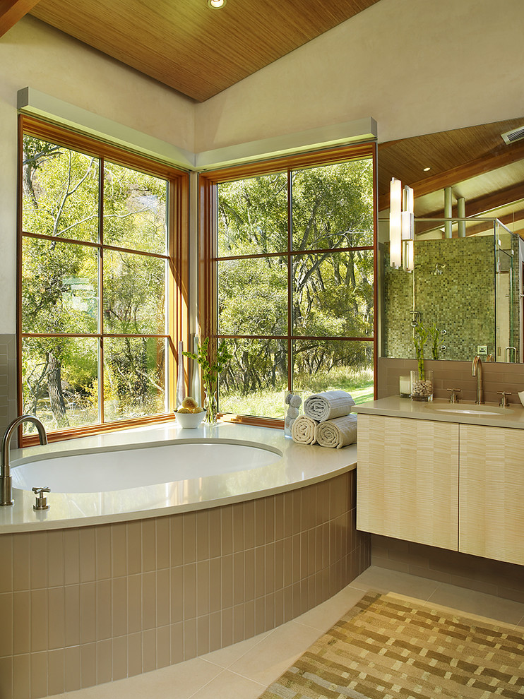 Cette photo montre une salle de bain tendance en bois clair avec un placard à porte plane, une baignoire encastrée et un carrelage beige.
