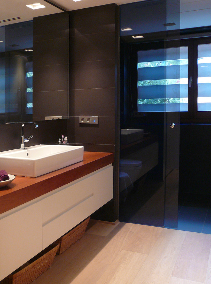 Foto på ett mellanstort funkis badrum med dusch, med luckor med upphöjd panel, vita skåp, en kantlös dusch, svarta väggar, ljust trägolv, ett fristående handfat och träbänkskiva