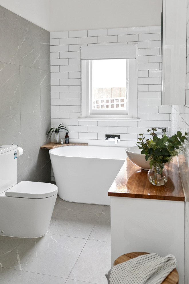 Modern inredning av ett mellanstort en-suite badrum, med ett fristående badkar, grå kakel, cementkakel, cementgolv, träbänkskiva och grått golv