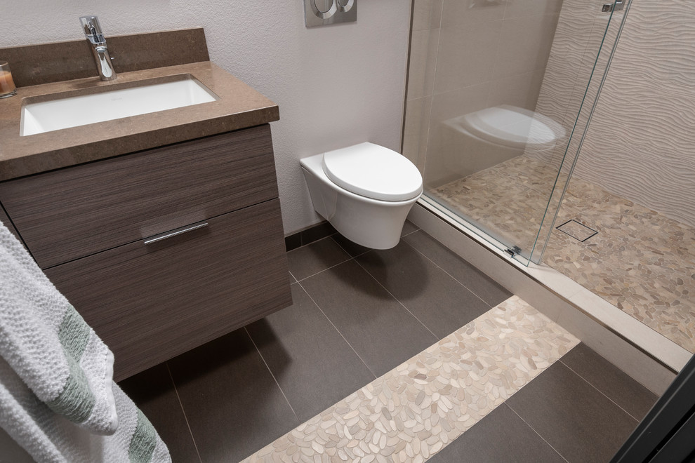 Bild på ett mellanstort funkis brun brunt badrum med dusch, med en kantlös dusch, en vägghängd toalettstol, beige kakel, porslinskakel, bruna väggar, klinkergolv i småsten, ett undermonterad handfat, bänkskiva i kvarts, brunt golv och dusch med skjutdörr