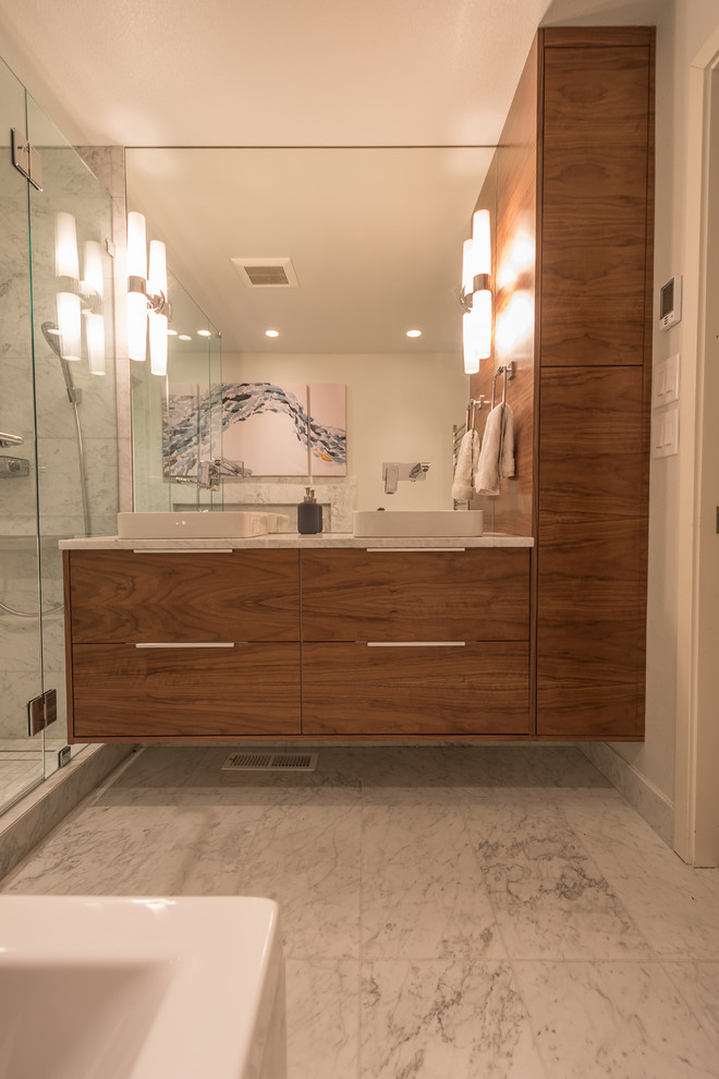 Cette image montre une salle de bain principale nordique en bois foncé de taille moyenne avec un placard à porte plane, une baignoire posée, une douche ouverte, un bidet, un carrelage gris, un carrelage de pierre, un mur gris, un sol en marbre, une vasque et un plan de toilette en marbre.