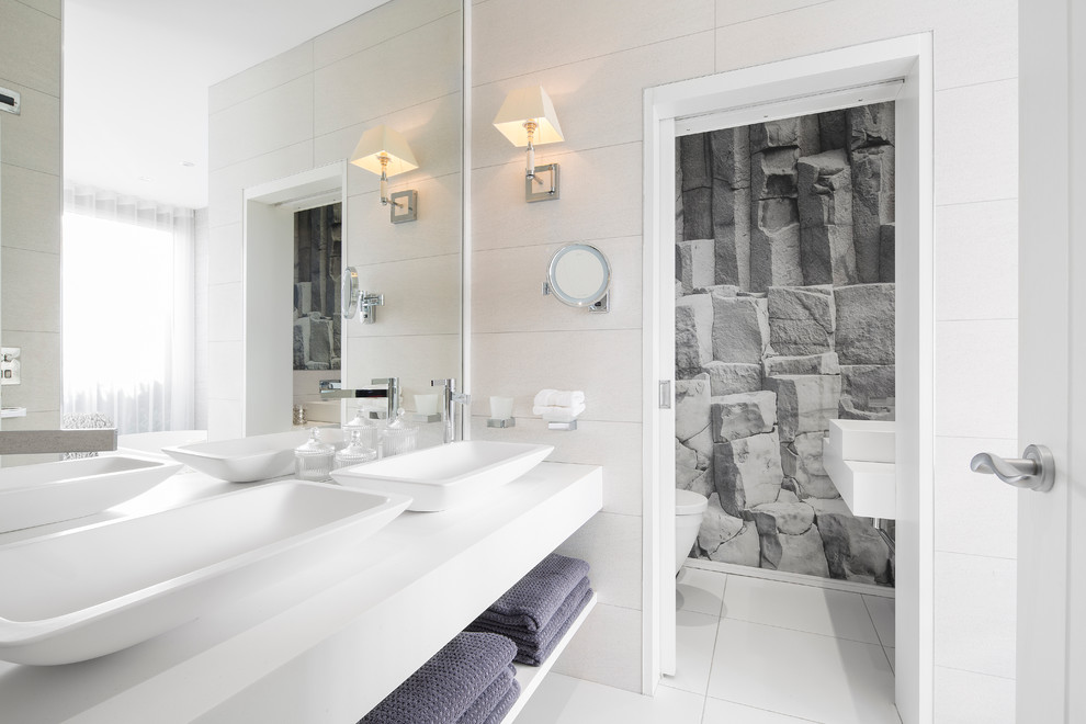 This is an example of a large contemporary grey and white ensuite bathroom in Other with open cabinets, a freestanding bath, white walls, a vessel sink, white cabinets, a built-in shower, a wall mounted toilet, white tiles, ceramic tiles, ceramic flooring, engineered stone worktops, white floors, a hinged door and white worktops.