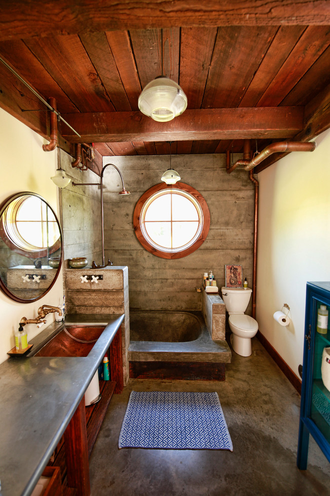 Inspiration för mellanstora industriella grått badrum med dusch, med öppna hyllor, skåp i mellenmörkt trä, en öppen dusch, en toalettstol med separat cisternkåpa, gula väggar, ett undermonterad handfat, ett platsbyggt badkar, betonggolv, bänkskiva i rostfritt stål, med dusch som är öppen, porslinskakel och brunt golv