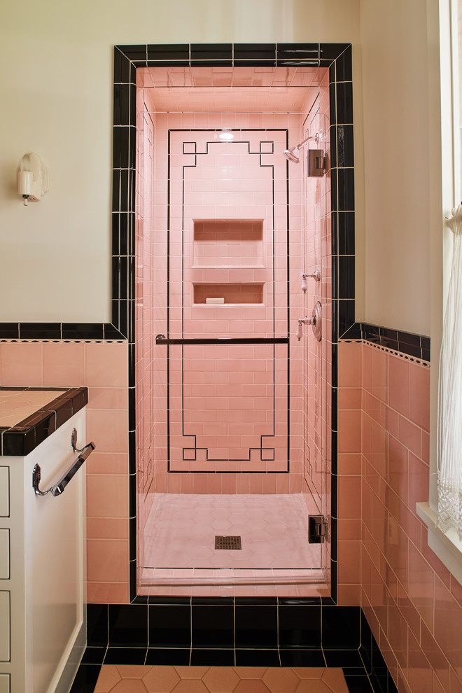 Foto på ett vintage badrum, med en dusch i en alkov, rosa kakel, rosa väggar, rosa golv, dusch med gångjärnsdörr och vita skåp