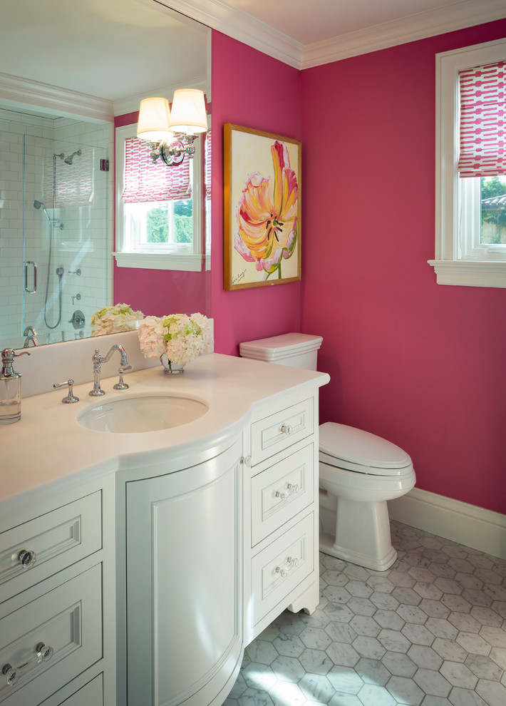 Modelo de cuarto de baño clásico de tamaño medio con paredes rosas, armarios tipo mueble, puertas de armario blancas, ducha empotrada, sanitario de dos piezas, suelo de mármol, lavabo bajoencimera y encimera de acrílico