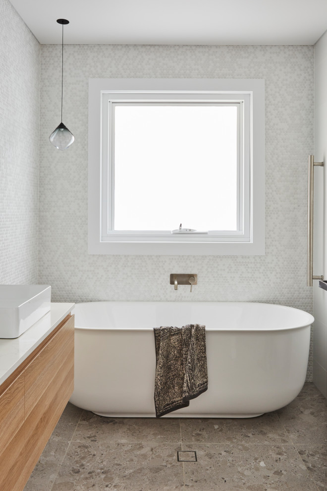 Exempel på ett skandinaviskt vit vitt badrum, med skåp i ljust trä, ett fristående badkar, en toalettstol med hel cisternkåpa, vit kakel, keramikplattor, vita väggar, klinkergolv i keramik, marmorbänkskiva och grått golv