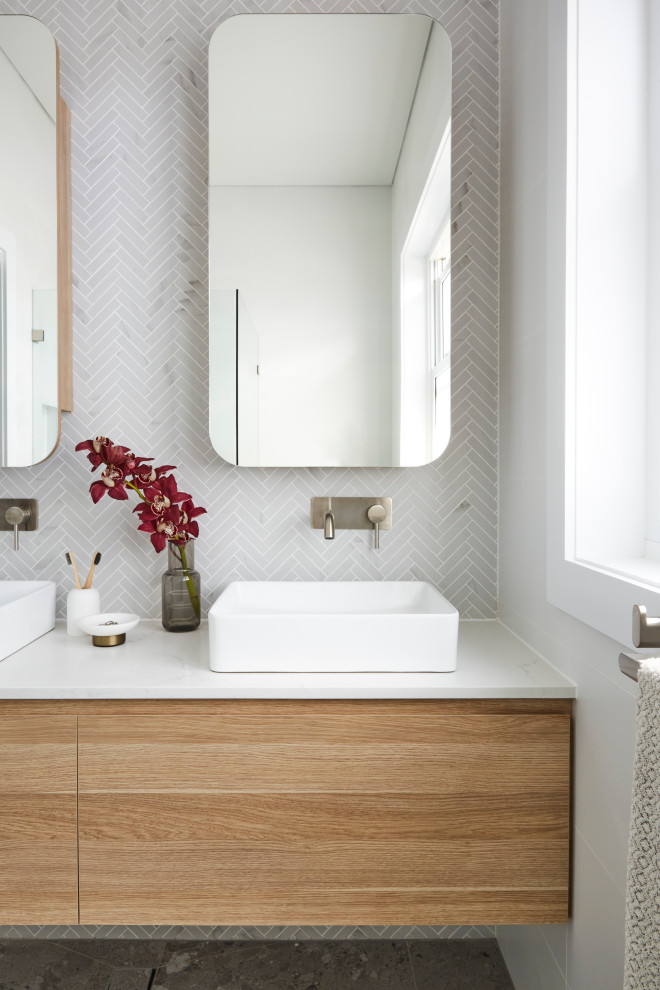 Foto på ett nordiskt vit badrum, med skåp i ljust trä, ett fristående badkar, en toalettstol med hel cisternkåpa, vit kakel, keramikplattor, vita väggar, klinkergolv i keramik, marmorbänkskiva och grått golv