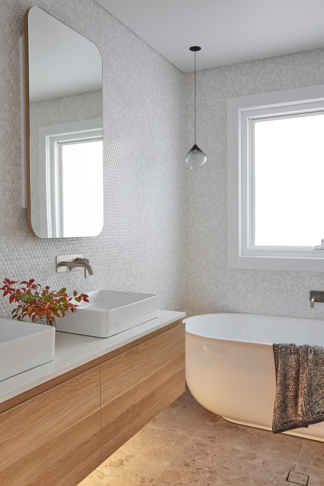 Cette photo montre une salle de bain scandinave en bois clair avec une baignoire indépendante, WC à poser, un carrelage blanc, des carreaux de céramique, un mur blanc, un sol en carrelage de céramique, un plan de toilette en marbre, un sol gris, un plan de toilette blanc, meuble double vasque et meuble-lavabo suspendu.