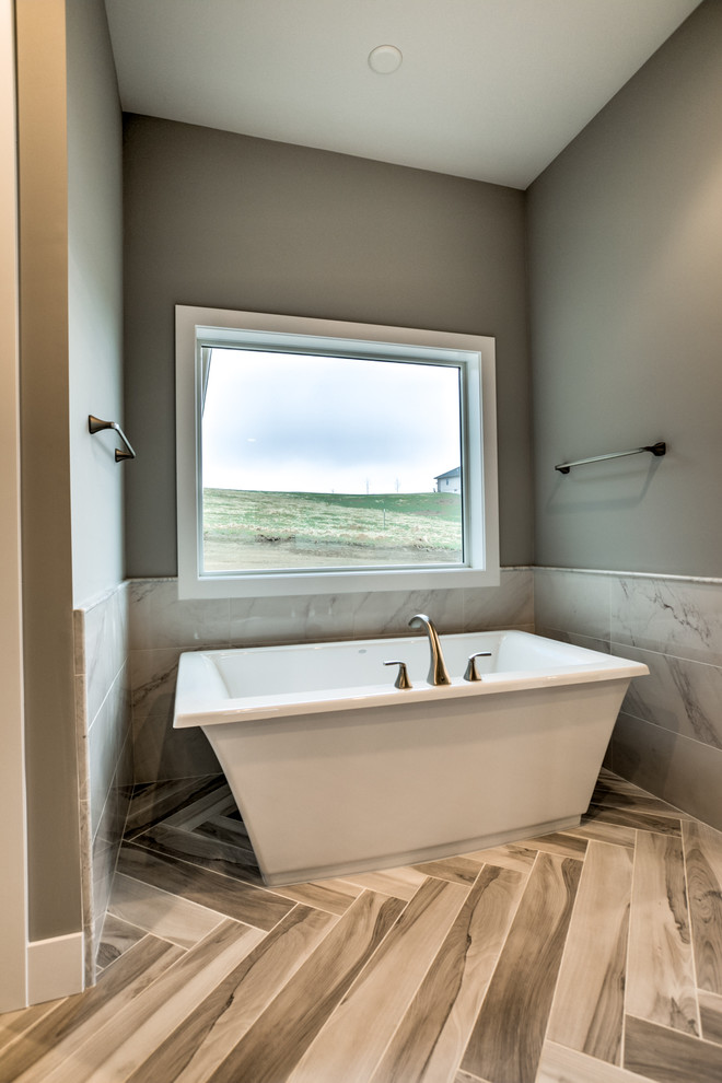 Inspiration for a large rural shower room bathroom in Omaha with shaker cabinets, a freestanding bath, porcelain flooring, grey cabinets, grey walls, a built-in sink, solid surface worktops, brown floors, a two-piece toilet and ceramic tiles.