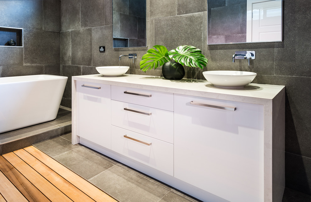 Inspiration for a large contemporary ensuite bathroom in Melbourne with flat-panel cabinets, white cabinets, a freestanding bath, a double shower, grey tiles, porcelain tiles, engineered stone worktops, an open shower, white worktops, a bidet, grey walls, porcelain flooring, a vessel sink and grey floors.
