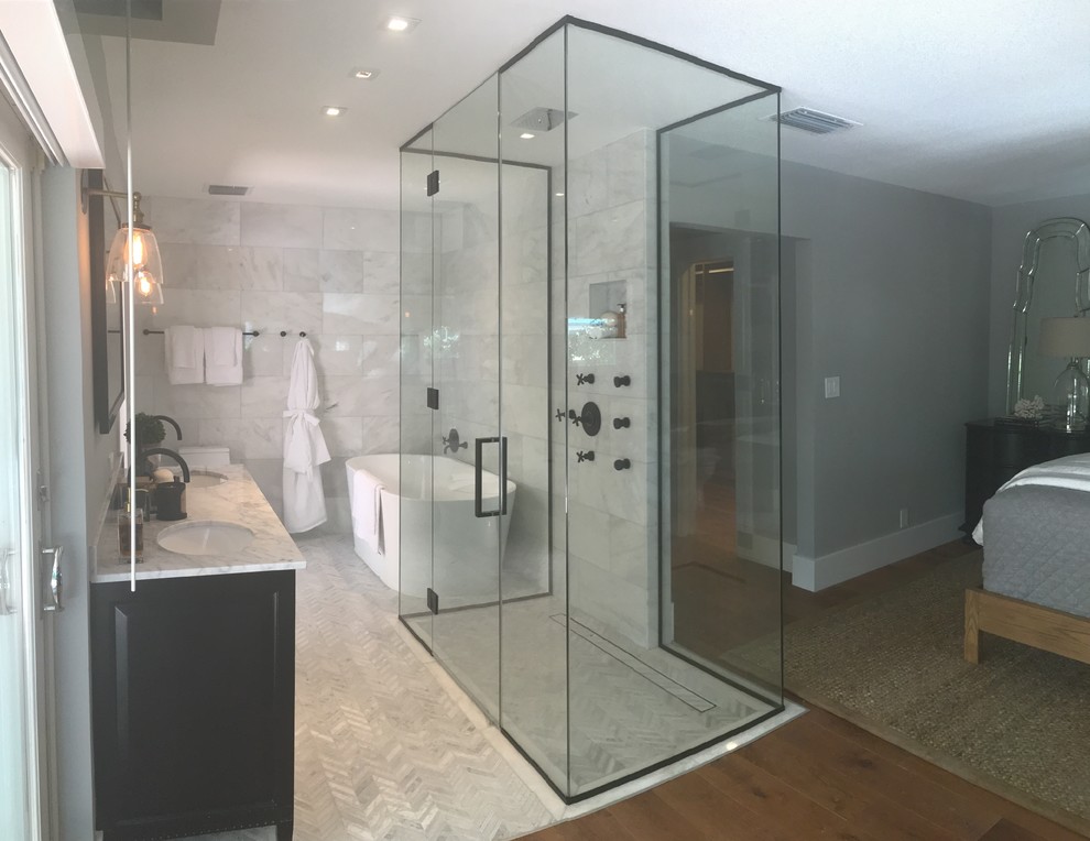 This is an example of a small modern ensuite bathroom in Tampa with dark wood cabinets, a freestanding bath, a corner shower, grey tiles, white tiles, marble tiles, beige walls, a submerged sink, a hinged door and grey worktops.