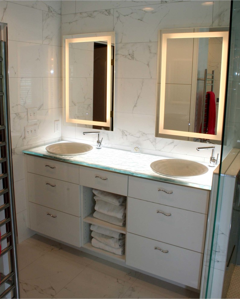 Cette image montre une salle de bain design avec un carrelage blanc, du carrelage en marbre, une vasque, un plan de toilette en verre et une cabine de douche à porte battante.