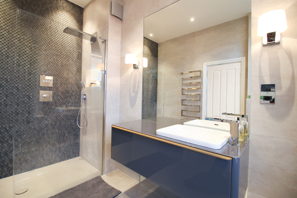 Medium sized modern ensuite bathroom in London with glass-front cabinets, grey cabinets, a walk-in shower, a wall mounted toilet, beige tiles, porcelain tiles, grey walls, porcelain flooring, a built-in sink, glass worktops, beige floors, an open shower and grey worktops.