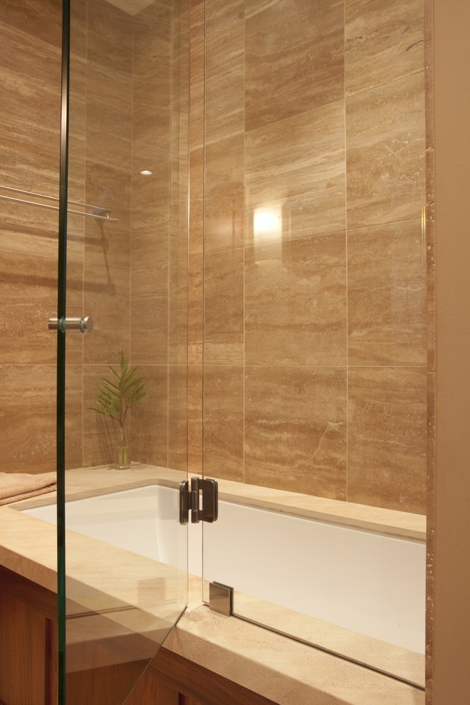 Пример оригинального дизайна: главная ванная комната среднего размера в стиле модернизм с темными деревянными фасадами, полновстраиваемой ванной, угловым душем, раздельным унитазом, серой плиткой, плиткой из известняка, бежевыми стенами, полом из керамогранита, столешницей из талькохлорита, бежевым полом, душем с распашными дверями и черной столешницей