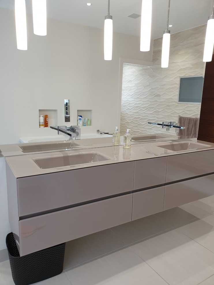 Идея дизайна: большая главная ванная комната в стиле модернизм с плоскими фасадами, коричневыми фасадами, бежевой плиткой, керамогранитной плиткой, монолитной раковиной, стеклянной столешницей и коричневой столешницей
