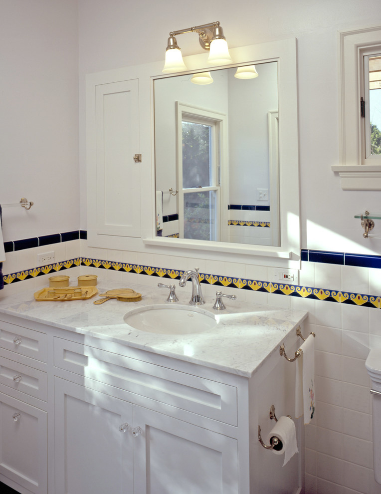 На фото: ванная комната среднего размера в классическом стиле с белыми фасадами, фасадами в стиле шейкер, белой плиткой, керамогранитной плиткой, врезной раковиной и мраморной столешницей с