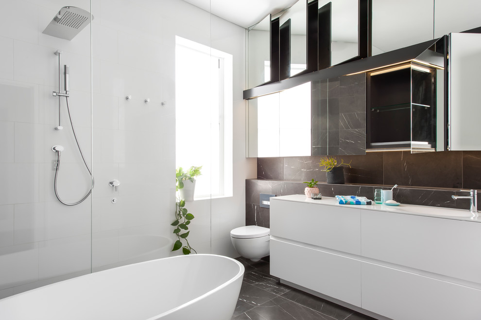 Inspiration för mellanstora moderna badrum med dusch, med möbel-liknande, vita skåp, ett fristående badkar, en öppen dusch, grå kakel, stenkakel, ett integrerad handfat och bänkskiva i akrylsten