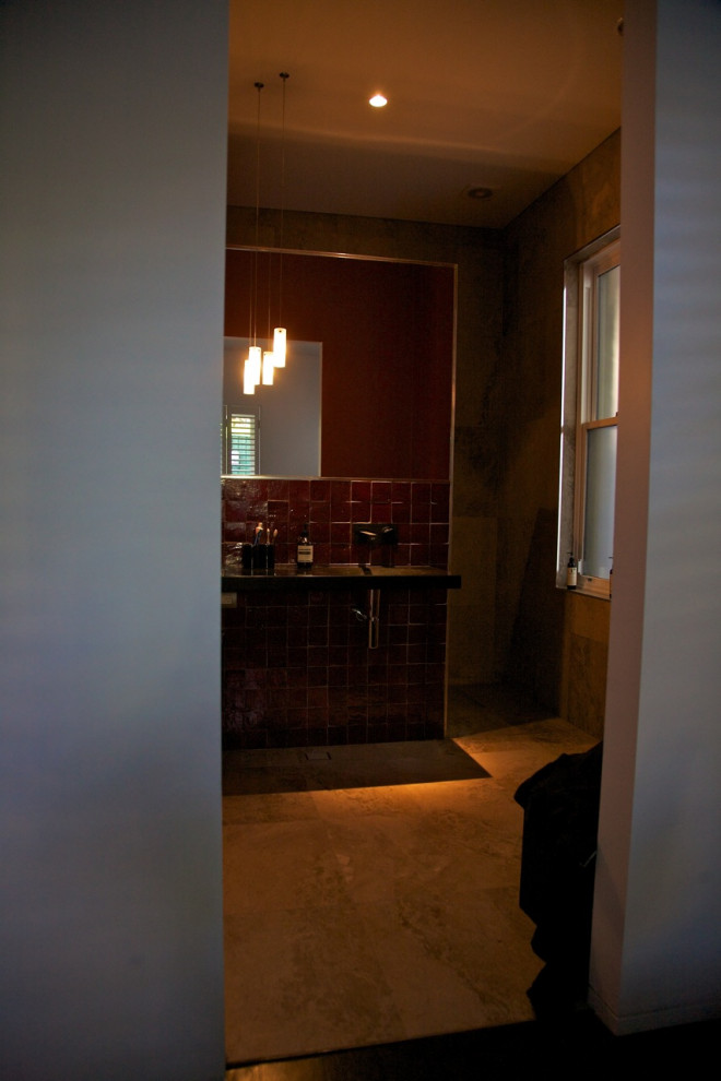 Modern inredning av ett stort svart svart en-suite badrum, med en dusch i en alkov, en vägghängd toalettstol, beige kakel, travertinkakel, röda väggar, travertin golv, ett väggmonterat handfat, bänkskiva i akrylsten, beiget golv och med dusch som är öppen