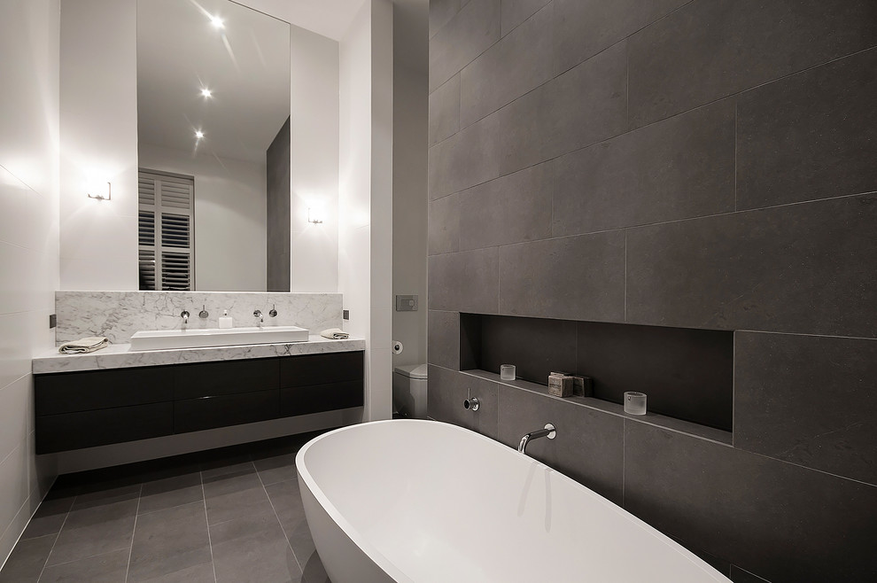 Идея дизайна: большая ванная комната в современном стиле с накладной раковиной, плоскими фасадами, темными деревянными фасадами, мраморной столешницей, отдельно стоящей ванной, унитазом-моноблоком, черной плиткой и белыми стенами