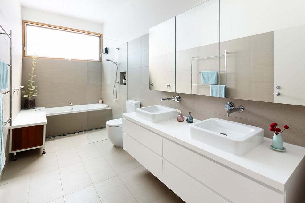メルボルンにあるコンテンポラリースタイルのおしゃれな浴室 (ドロップイン型浴槽、オープン型シャワー、セラミックタイルの床、グレーの壁、グレーのタイル、オーバーカウンターシンク、フラットパネル扉のキャビネット、白いキャビネット、オープンシャワー) の写真