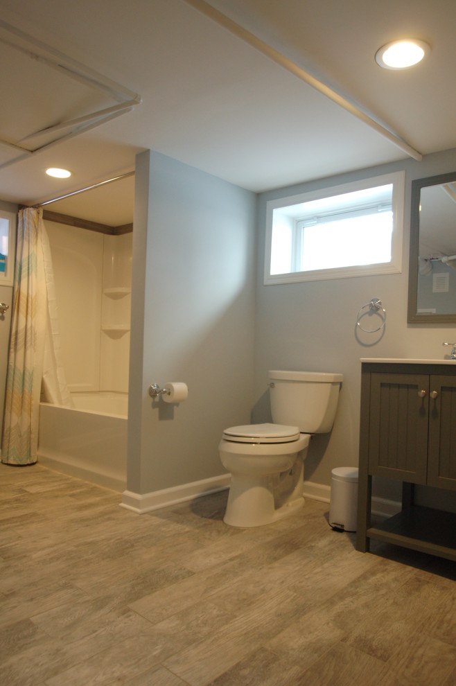 Inredning av ett klassiskt mellanstort badrum, med ett integrerad handfat, luckor med profilerade fronter, grå skåp, bänkskiva i kvarts, ett badkar i en alkov, en dusch/badkar-kombination, en toalettstol med separat cisternkåpa, grå kakel, porslinskakel, grå väggar, klinkergolv i porslin, beiget golv och dusch med duschdraperi