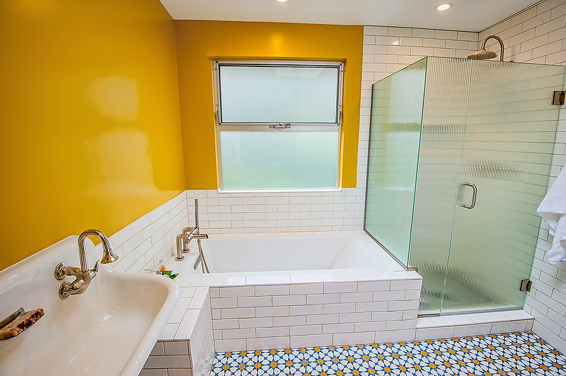Пример оригинального дизайна: ванная комната среднего размера в стиле ретро с открытыми фасадами, раздельным унитазом, белой плиткой, душевой кабиной, столешницей из искусственного камня, полновстраиваемой ванной, угловым душем, каменной плиткой, желтыми стенами, полом из цементной плитки, раковиной с несколькими смесителями, синим полом и душем с распашными дверями