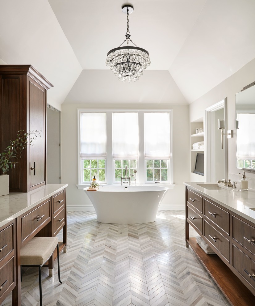 Modelo de cuarto de baño principal clásico renovado con armarios con paneles lisos, puertas de armario de madera en tonos medios, bañera exenta, paredes blancas, lavabo tipo consola, suelo gris y encimeras blancas