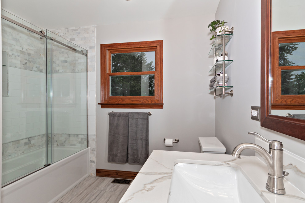 Photo of a medium sized traditional ensuite bathroom in Chicago with freestanding cabinets, dark wood cabinets, an alcove bath, a shower/bath combination, a two-piece toilet, white tiles, marble tiles, grey walls, ceramic flooring, a submerged sink, engineered stone worktops, beige floors, a sliding door and beige worktops.